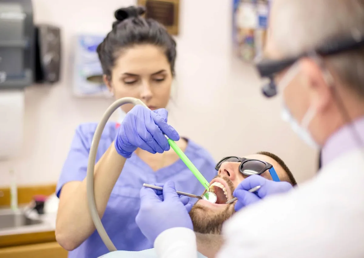 Dentist and dental assistant removing plaque from a patient’s teeth during a professional cleaning.